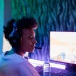 Teenage boy engaged in online gaming with headphones in a dimly lit room.