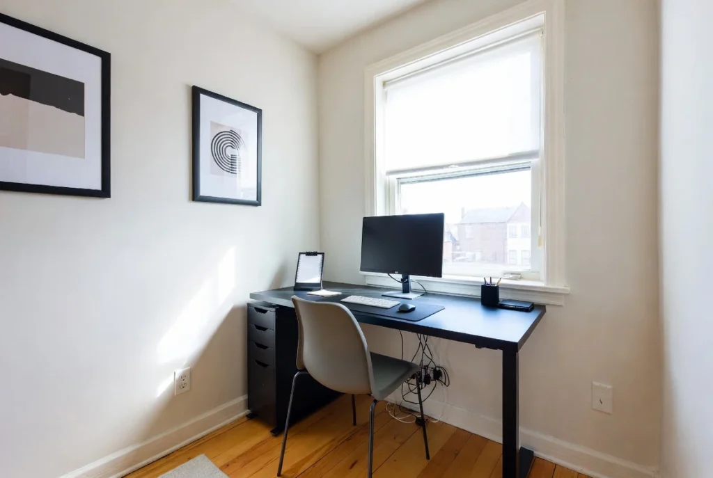 Desk positioned near window in small apartment workspace with natural light reducing eye strain